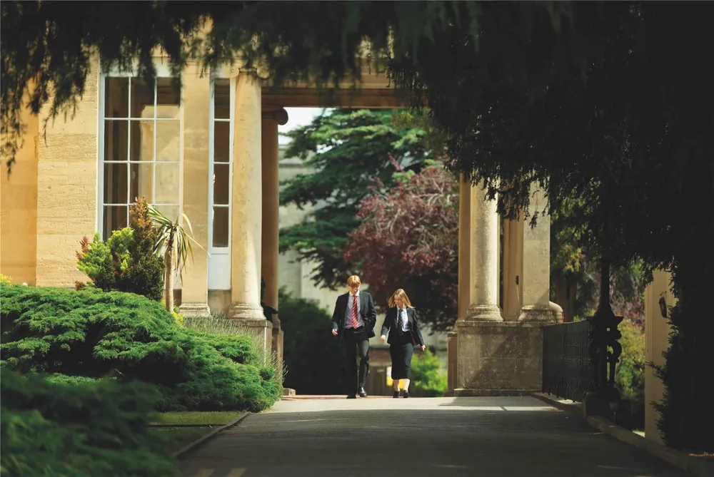 Cheltenham College – Zwei Schüler in Uniform spazieren durch einen begrünten Säulengang