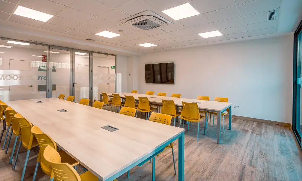 Yago School Sevilla – Heller Lernraum mit langen Tischen und farbigen Stühlen