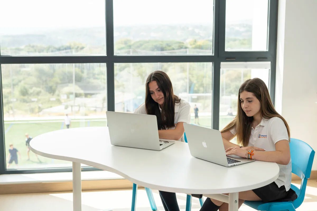 Zwei Schülerinnen arbeiten an Laptops in der Sotogrande International School mit Blick auf die Sportplätze